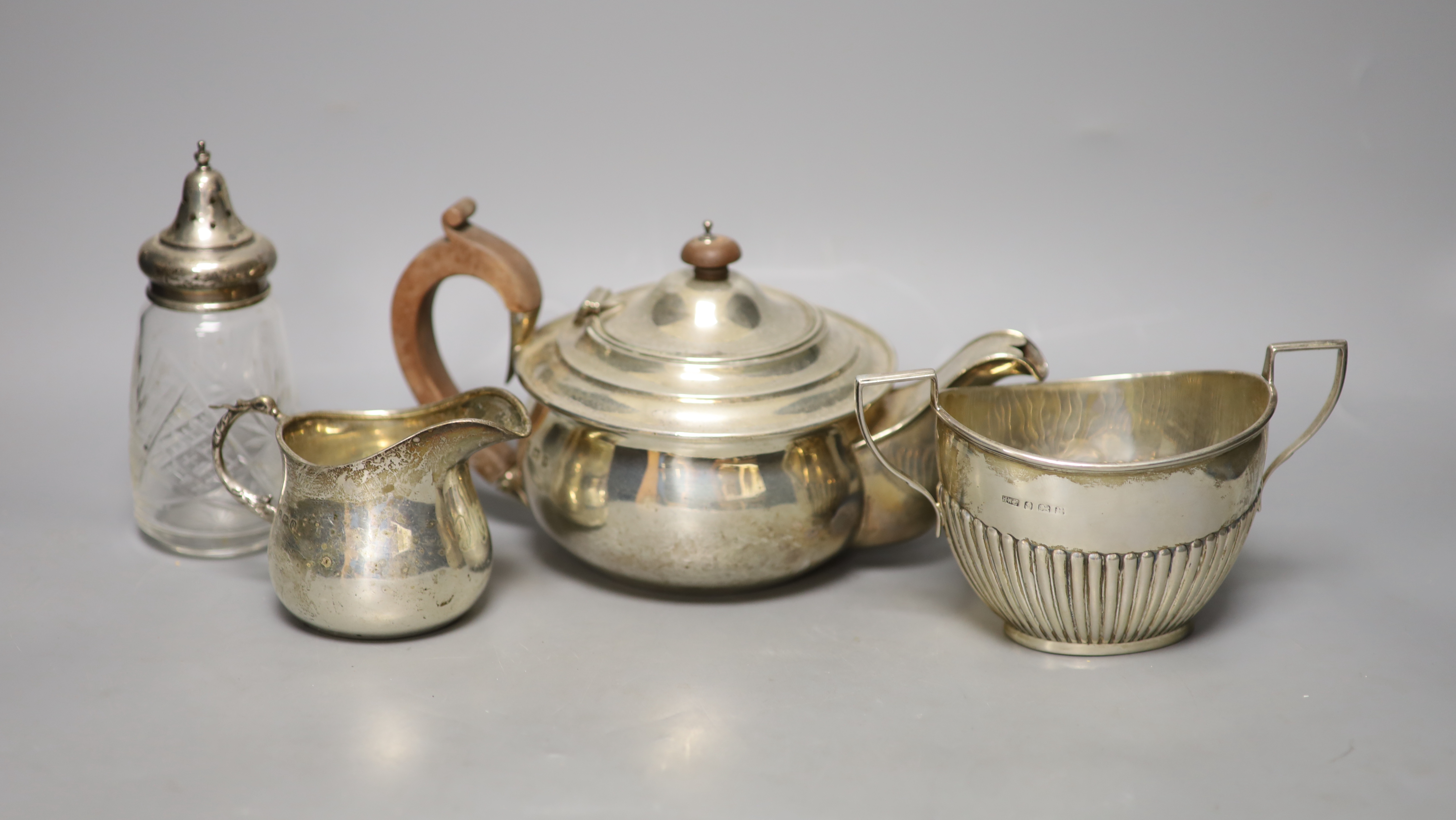 A George V silver teapot, Birmingham, 1913, a similar cream jug and sugar bowl and a silver mounted glass sugar sifter